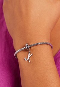 Zilveren armband met een flexibele ontwerp, voorzien van een hangende charme in de vorm van een "x" en verfraaid met een kleine heldere edelsteen.