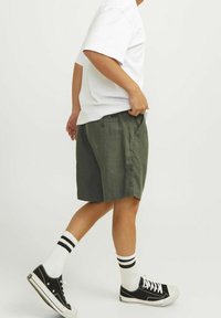 Gröna shorts med en avslappnad passform, tillverkade av lättviktsmaterial, matchade med en vit t-shirt och svarta sneakers med vita randiga strumpor.