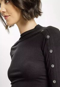 Czarny, prążkowany top z długim rękawem, z srebrnymi zatrzaskami wzdłuż szwu na ramieniu, o dopasowanym kroju i wysokim kołnierzu.