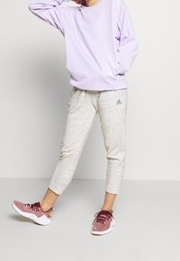Fialová mikina s dlouhým rukávem, šedé cropped tepláky a vínové pletené sportovní boty s bílou podešví. Výrazná loga Adidas jsou přítomna.