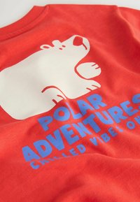 Tessuto rosso con un orso polare cartonato bianco e testo blu che legge "AVVENTURE POLARI" e testo più piccolo parzialmente visibile sotto.