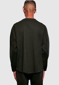 Schwarzes Langarm-Cotton-T-Shirt mit abgerundetem Saum, überschnittenen Schultern und Rundhalsausschnitt, das eine glatte Textur und eine lockere Passform bietet.
