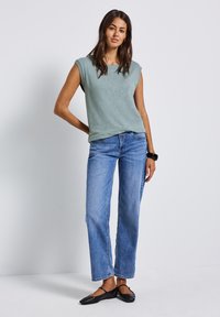 Jasnozielona bluzka z krótkim rękawem zestawiona z niebieskimi, szerokimi dżinsami i czarnymi płaskimi butami. Bluzka ma luźny krój i subtelną strukturę.