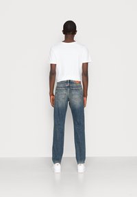 Siniset denimi farkut, suora leikkaus, haalistunut pinta, viisi taskua ja nahkainen merkki takana, yhdistetty yksinkertaiseen valkoiseen t-paitaan.