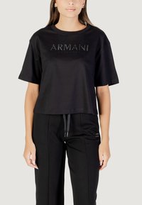 Camiseta corta negra de algodón con mangas cortas. Presenta "ARMANI EXCHANGE" en texto brillante en el pecho.