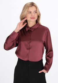 Bluza din satin burgundy cu un guler structurat și mâneci lungi, având un închidere cu nasturi în față și o textură netedă și lucioasă.