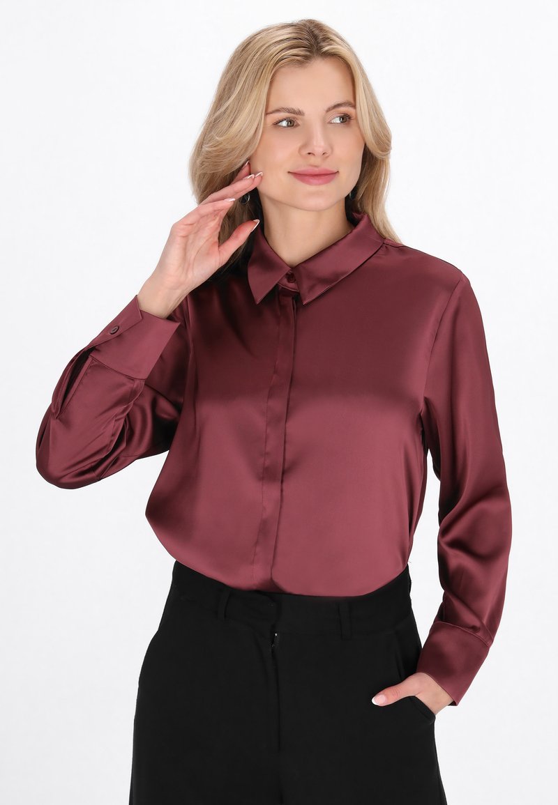 Bluza din satin burgundy cu un guler structurat și mâneci lungi, având un închidere cu nasturi în față și o textură netedă și lucioasă.