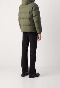 Grön vadderad jacka med huva, med ett kviltat mönster. Kombinerad med svarta raka jeans och svarta skor, sedd bakifrån.