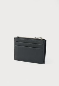 Portefeuille en cuir noir avec fermeture éclair, plusieurs emplacements pour cartes et texture lisse. Design rectangulaire compact avec des détails de coutures fines.
