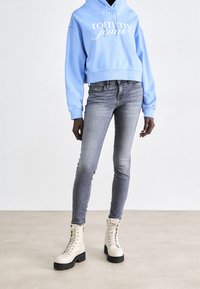 Sudadera corta azul claro con el logo "Tommy Jeans", combinada con jeans ajustados grises y botas de combate beige con cordones y suelas negras.