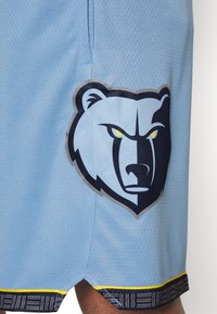 Jasnoniebieskie szorty sportowe z oddychającą siateczką mają ciemnoniebieskie logo misia, podkreślone �żółtymi i wzorzystymi lamówkami na dolnym brzegu.