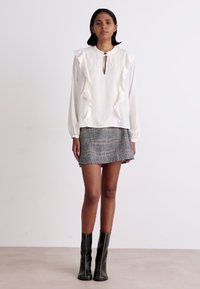 Balta blūze ar rufļu detaļām un atslēgvārdu kakla izgriezumu, apvienota ar pelēku raibi svārku mini garumā. Modelis valkā melnas ceļgala zābakus.