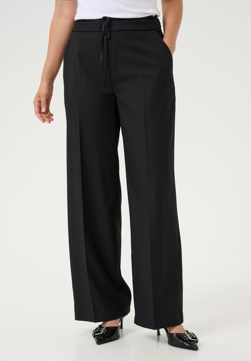 Pantaloni negri cu pantaloni largi, cu un cordon la talie, buzunare laterale și o textură netedă, asortați cu tocuri negre cu vârful ascuțit.