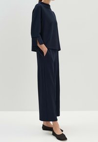 Top azul marino con mangas tres cuartos y cuello alto, combinado con pantalones de pierna ancha; ambos en una tela ligera. Zapatos planos negros.