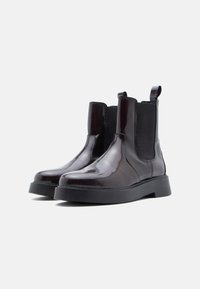Botas Chelsea de charol negro con paneles laterales elásticos, punta redondeada y una suela gruesa negra. Textura suave con un diseño elegante.