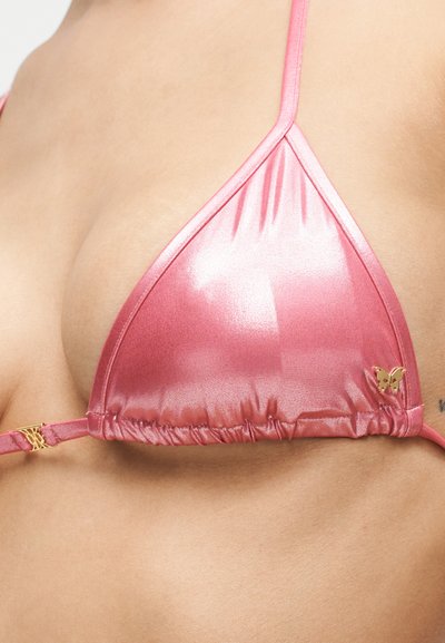 Prim-plan cu un top de bikini din satin roz, cu bretele subțiri și o mică decorațiune aurie în formă de fluture pe cupa dreaptă.