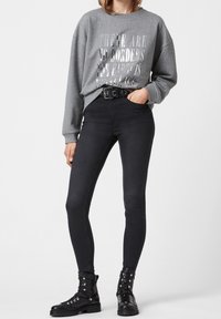Sudadera gris con texto reflectante plateado, combinada con unos jeans skinny negros y unas botas de tobillo negras con cordones y detalles metálicos.