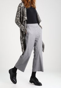 Grå vida byxor med en slät yta, tillsammans med en svart-och-vit randig kofta. Svarta snörskor kompletterar outfiten.