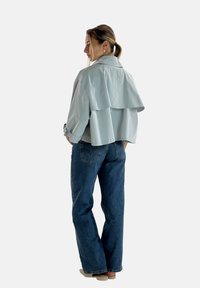 Lyseblå jakke med lagdelt rygdesign, lange ærmer og blød tekstur, parret med højtaljede mørkeblå jeans.