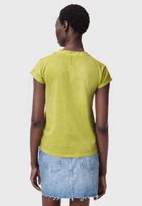 Krótki rękaw, limonkowa bluzka wykonana z lekkiego materiału. Posiada prosty wygląd, okrągły dekolt i podwinięte mankiety.
