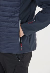 Marinejakke med quiltet front, glat ryg, to lynlåslommer og røde hardware-detaljer. Har justerbar kant og broderet logo.