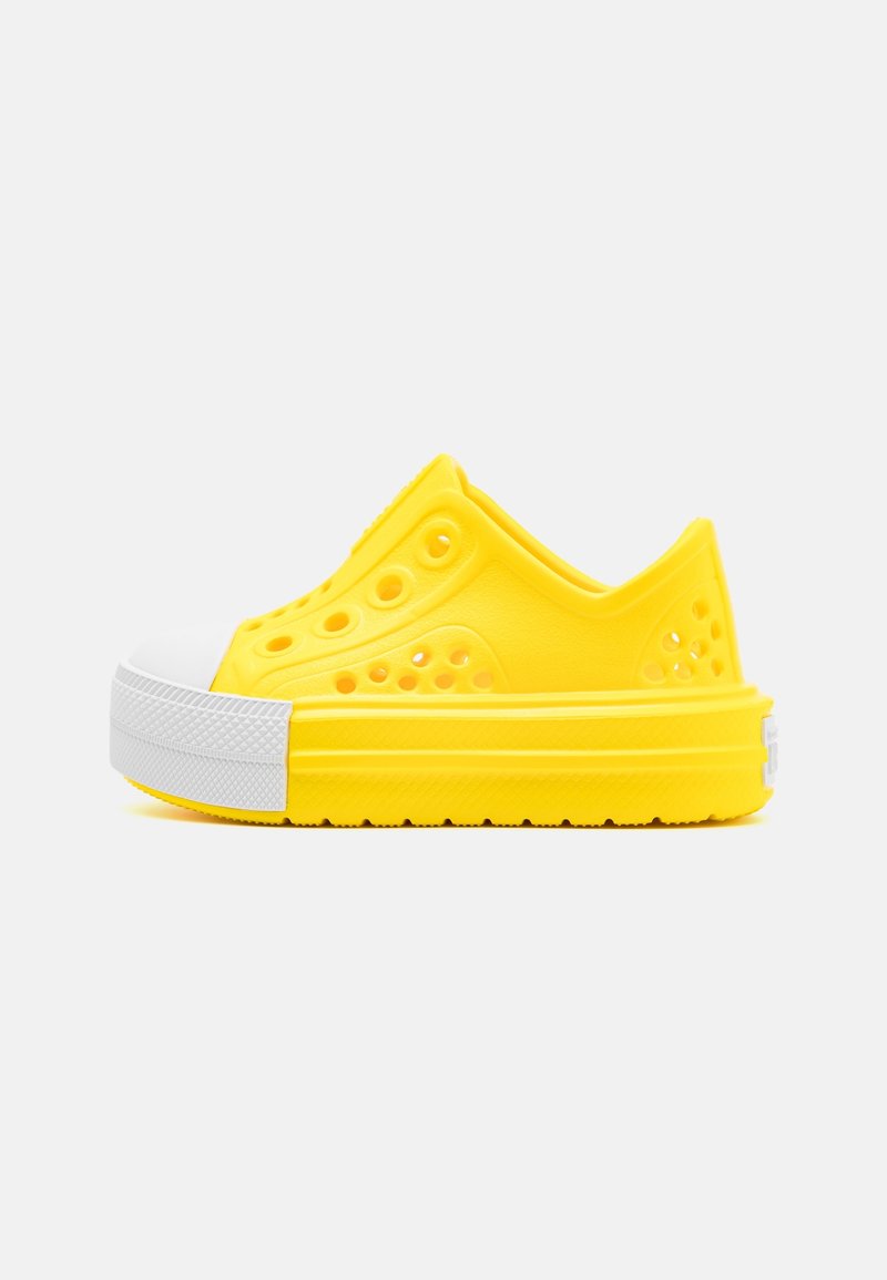 Chaussure en caoutchouc jaune à enfiler avec des trous de ventilation et un gros embout texturé blanc, vue de profil sur un fond uni.