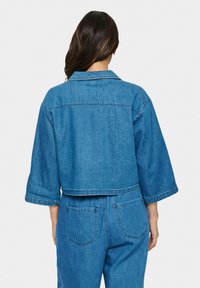 Džinsasta jakna s skrajšanim dizajnom, širokimi rokavi in šilastim ovratnikom. Ima enotno modro barvo in vidne šive.