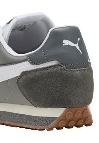 Zapatillas grises con una mezcla de texturas de cuero liso y gamuza, con una franja blanca y suela de goma con patrones circulares.