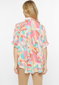 Colorful, lightweight blouse featuring an abstract geometric pattern in pastel shades of pink, blue, and orange. Short sleeves with a relaxed fit.