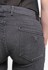 Úzké černé džíny z denimu s texturovaným povrchem, na kterých je trojúhelníková nášivka a dvě zadní kapsy.