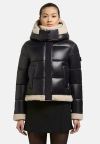 Schwarze Pufferjacke mit cropped Design, ausgestattet mit einem beigen Kunstfellkragen und -manschetten sowie schrägen Seitentaschen. Glatte, glänzende Oberfläche.