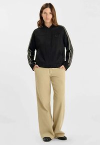 Svart kavaj med kritstrecksrand och hög krage, med vita ränder på ärmarna. Matchad med beige vida byxor och svarta skor.