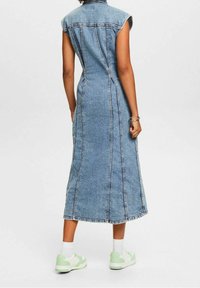 Denim maxiklänning med korta ärmar, med vertikala sömmar, en figurnära liv och en utsvängt kjol. Bärs med mintgröna sneakers.