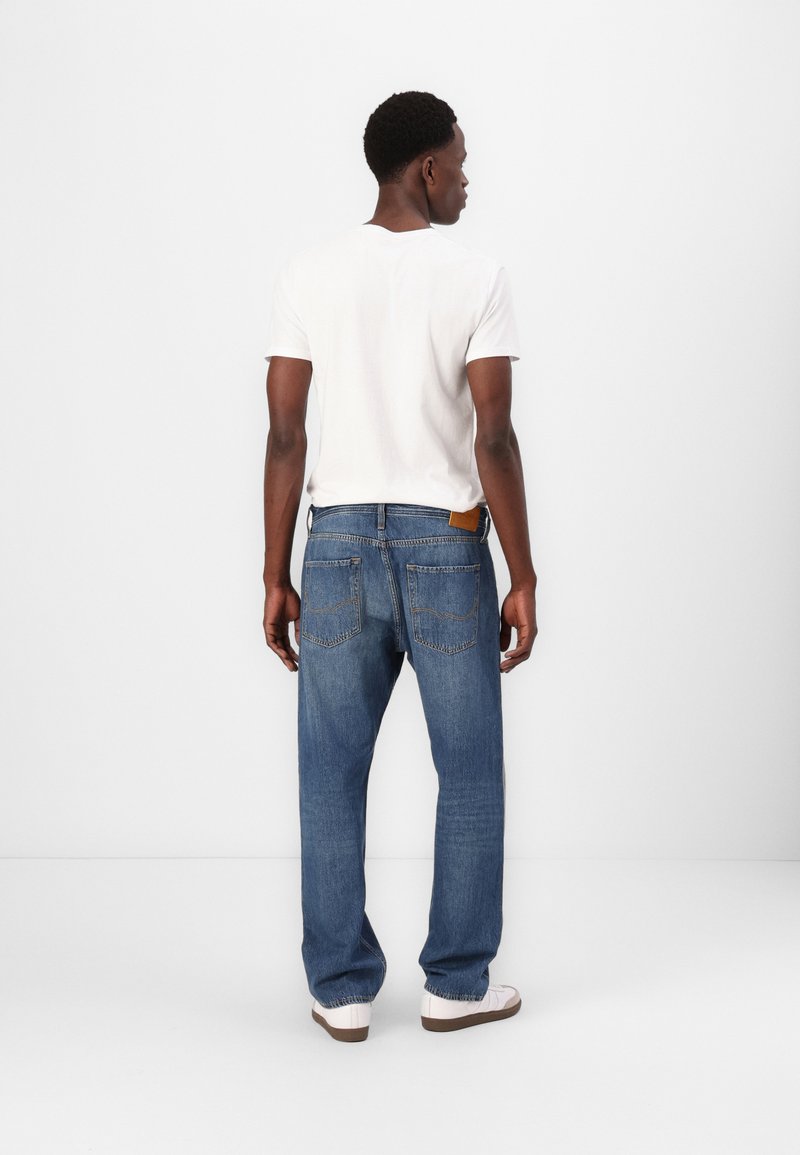 Blaue Denim-Jeans mit lockerem Schnitt, sichtbaren Gesäßtaschen und einem braunen Lederetikett am Bund. Kombiniert mit einem schlichten weißen T-Shirt.