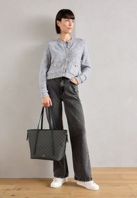 Cardigan lavorato a maglia blu con texture e bottoni dorati, jeans grigi a gamba larga e una borsa a tracolla nera con motivo. Le sneakers bianche completano l'outfit.