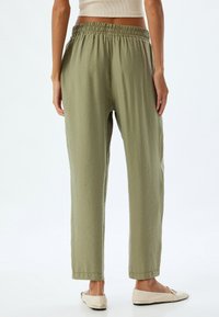 Olijfgroene elastische taillebroek met een comfortabele pasvorm, een gladde textuur, zijzakken en taps toelopende benen, gecombineerd met crèmekleurige platte schoenen.