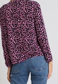 Leopardmönstrad topp i rosa och svart; långärmad; rundad fåll; kombinerad med blå denimjeans med fickor och figurnära passform.