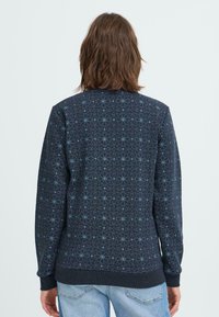 Sweat-shirt navy arboré d'un motif de étoiles géométriques bleu clair, avec des poignets et un ourlet côtelés, et une coupe décontractée. Vue arrière affichée.