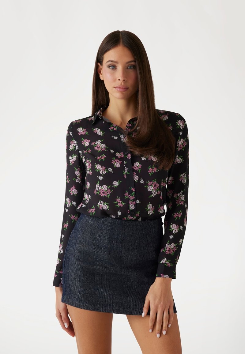 Blusa nera floreale con maniche lunghe e colletto, decorata con piccoli fiori rosa e bianchi; abbinata a una mini gonna in denim scuro.