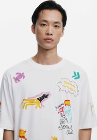 Witte katoenen T-shirt met kleurrijke abstracte prints, waaronder dieren en tekst, met een relaxed fit en ronde hals.