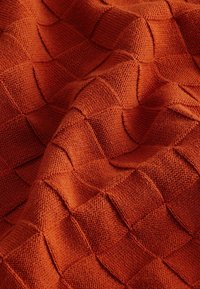 Tissu tricoté en orange profond avec un motif texturé de carrés en relief, montrant une apparence douce et chaleureuse.