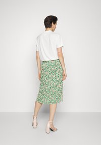 T-shirt branca de mangas curtas combinado com uma saia floral verde até ao joelho, apresentando flores em rosa e amarelo, complementado com sandálias de salto bloco em rosa claro.