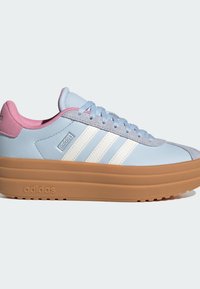 Baskets Adidas bleu clair avec des rayures blanches, une doublure intérieure rose, des lacets gris et une semelle épaisse en caoutchouc marron.