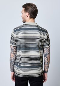 Pruhovaná polo tričko v béžové a námořnické modře, s krátkými rukávy a klasickým límcem. Tkanina je měkká, s přiléhavým střihem a jemným akcentovým prošíváním.