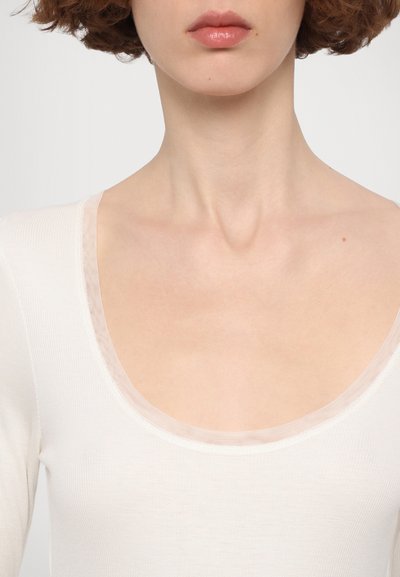 White ribbed long-sleeve top featuring a round neckline with a sheer trim, smooth texture, and fitted silhouette.