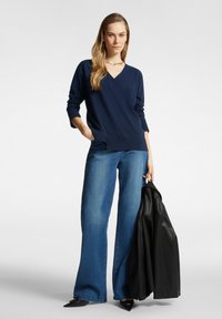 Suéter de punto azul marino con escote en V, combinado con jeans de pierna ancha y una chaqueta de cuero negra. Tejido suave y corte relajado con mangas largas.