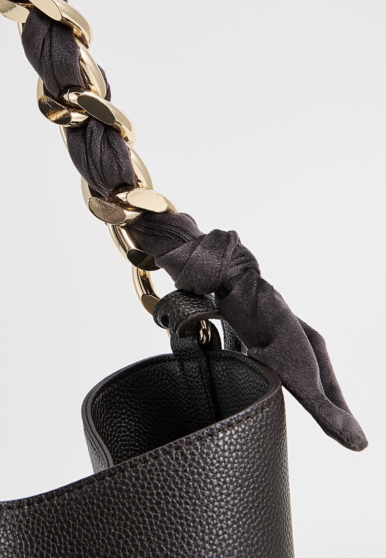 Czarna skórzana torebka o teksturowanym wykończeniu, z złotym łańcuszkiem i ciemnym materiałowym akcentem związanym do uchwytu.