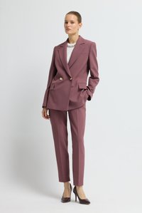 Blazer de doble botonadura y pantalones ajustados de tela malva. El blazer presenta botones dorados y bolsillos frontales. Se lleva con tacones oscuros.