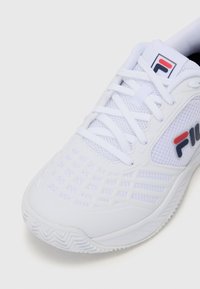 Scarpa atletica bianca con tomaia in rete, motivo testurizzato sui lati, suola in gomma e logo ricamato in rosso e blu. I lacci sono bianchi.