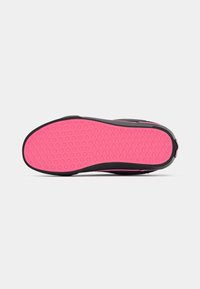 Baskets noires avec semelle texturée rose vif présentant des motifs de losanges et de cercles, vues par le dessous.